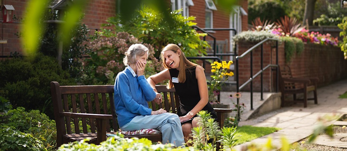 Care home manager sat on a bench laughing with resident in the garden