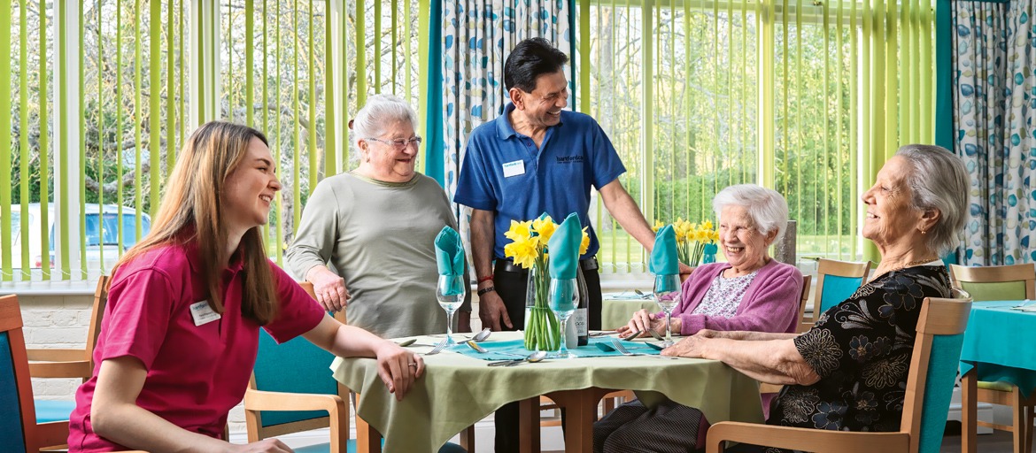 Residents and carers sat around a table in the dinning room all laughing and smiling