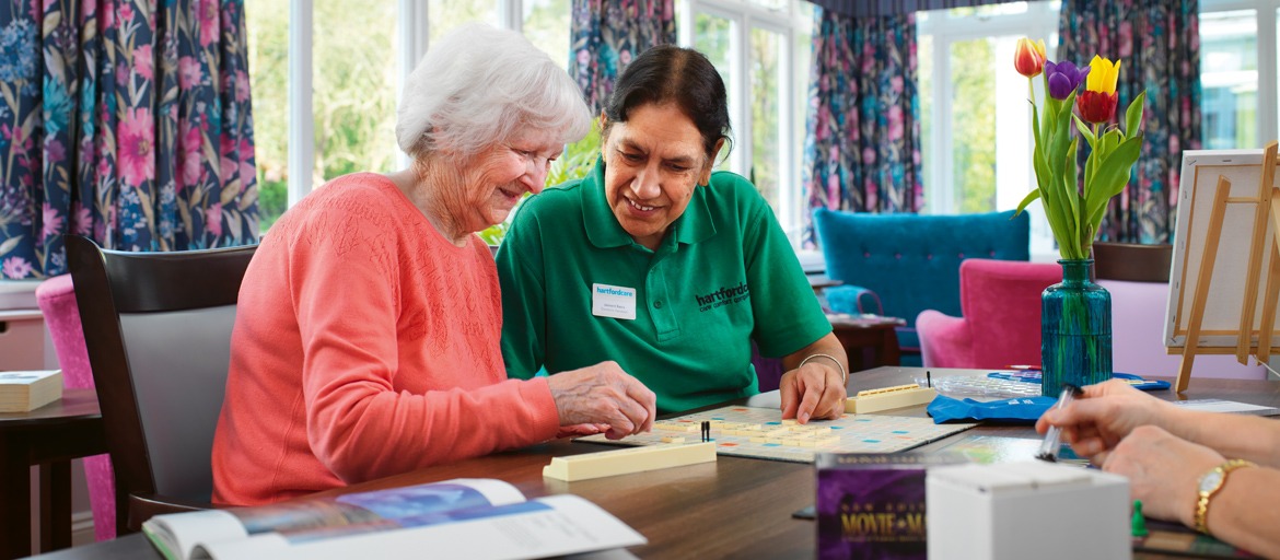 Carer and resident playing scrabble together at the table in the activities room
