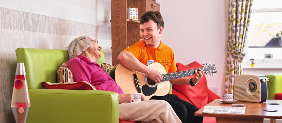 care assistant playing guitar to resident