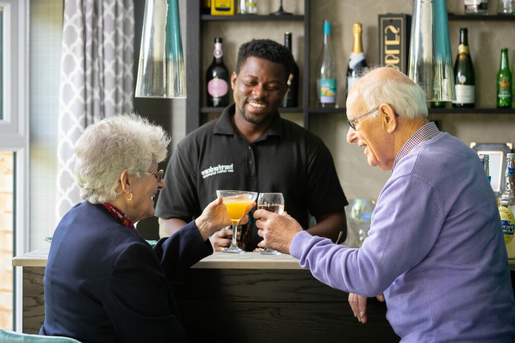 Two residents being served drinks by a barman at the bar area within Care Home