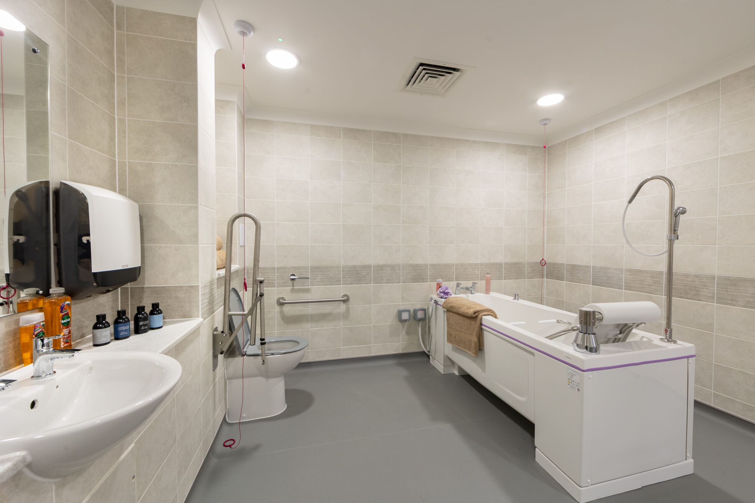 Spacious assisted living bathroom at Moorhill Care Home featuring a centrally placed bath, toilet, and wash basin with accessibility features