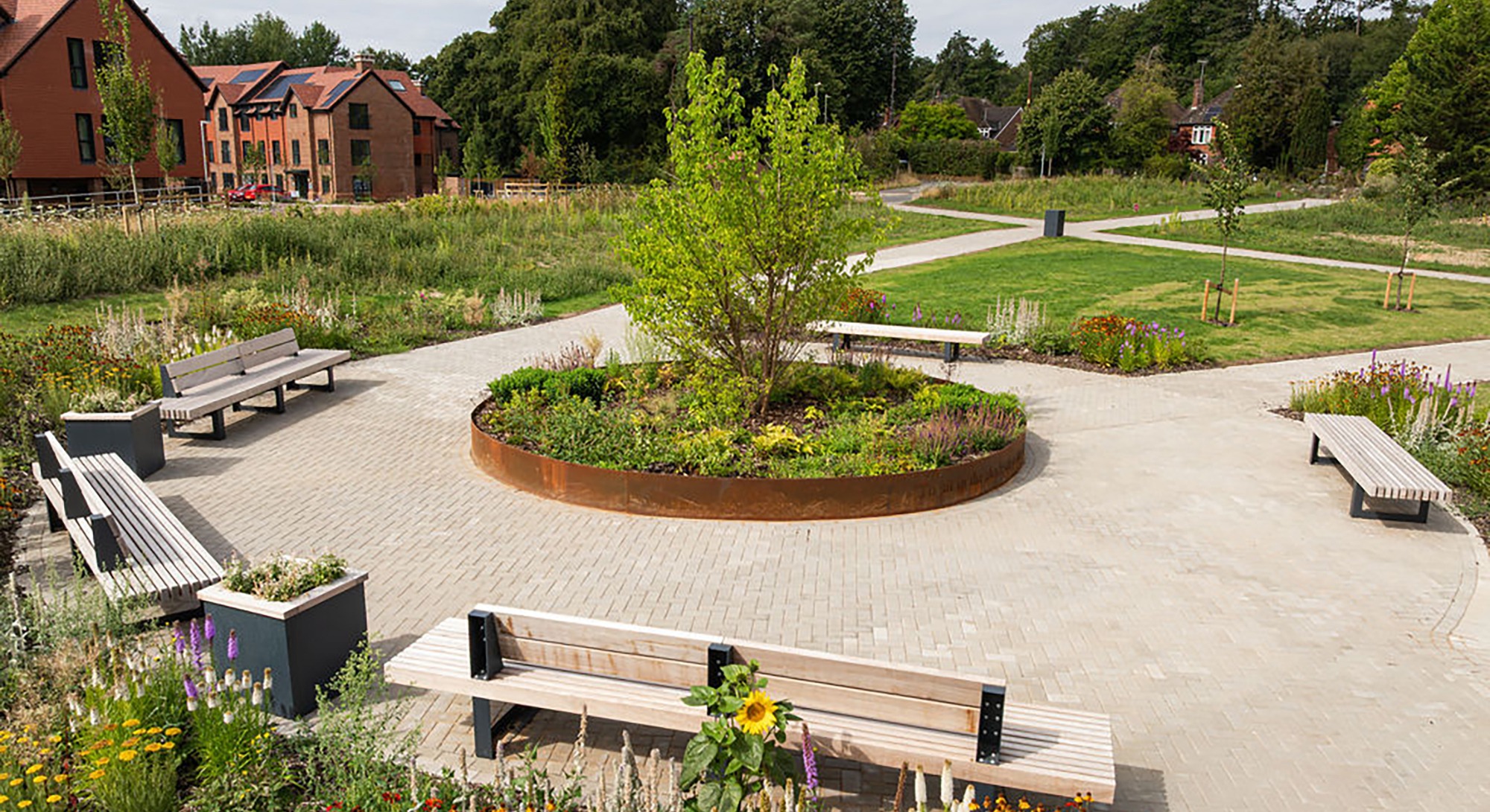 Aerial drone image of Alton Place Care Home garden, showing a raised circular flower bed with tree, surrounding circular path, benches for residents, and the care home building in the background