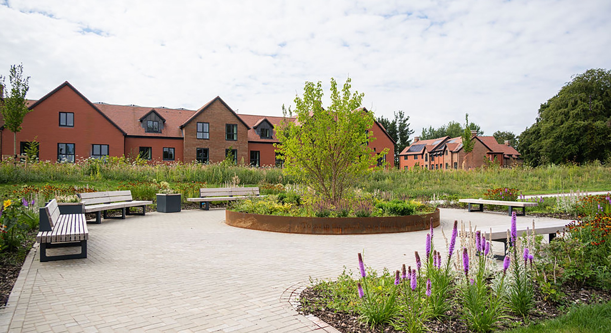 Landscaped garden at Alton Place Care Home with a raised circular flower bed and tree in the centre, surrounded by a circular path and benches for residents