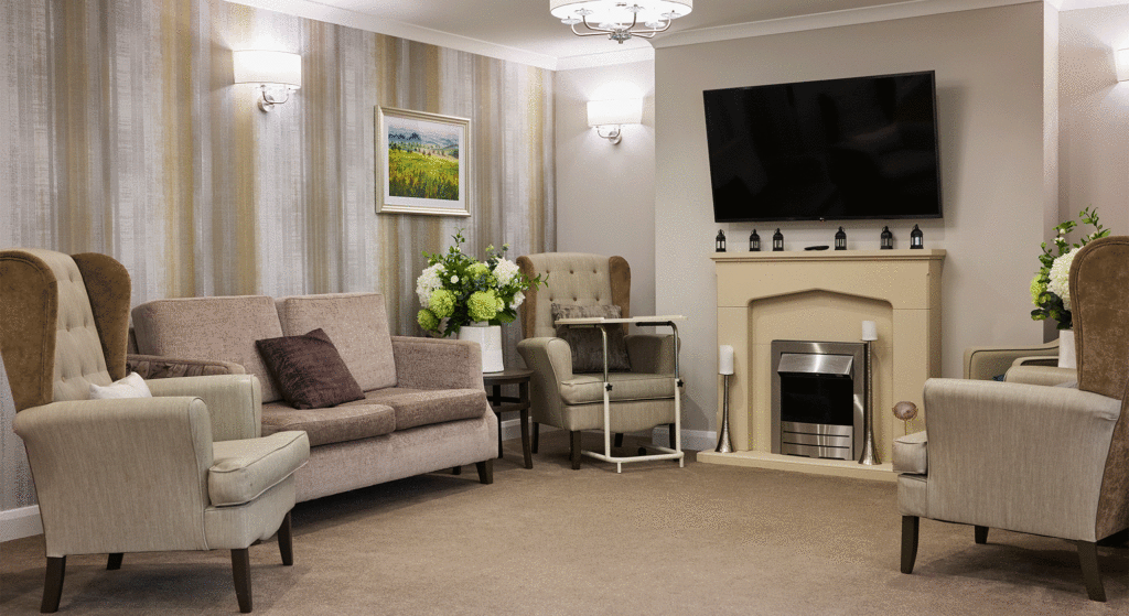 Living room at Cotswolds Rise Care Home in Swindon with three armchairs and a sofa arranged around a fireplace
