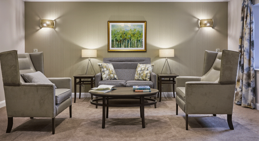 Sitting area at Cotswolds Rise Care Home in Swindon with two armchairs, a small sofa, coffee table, and warm lighting creating a cosy atmosphere