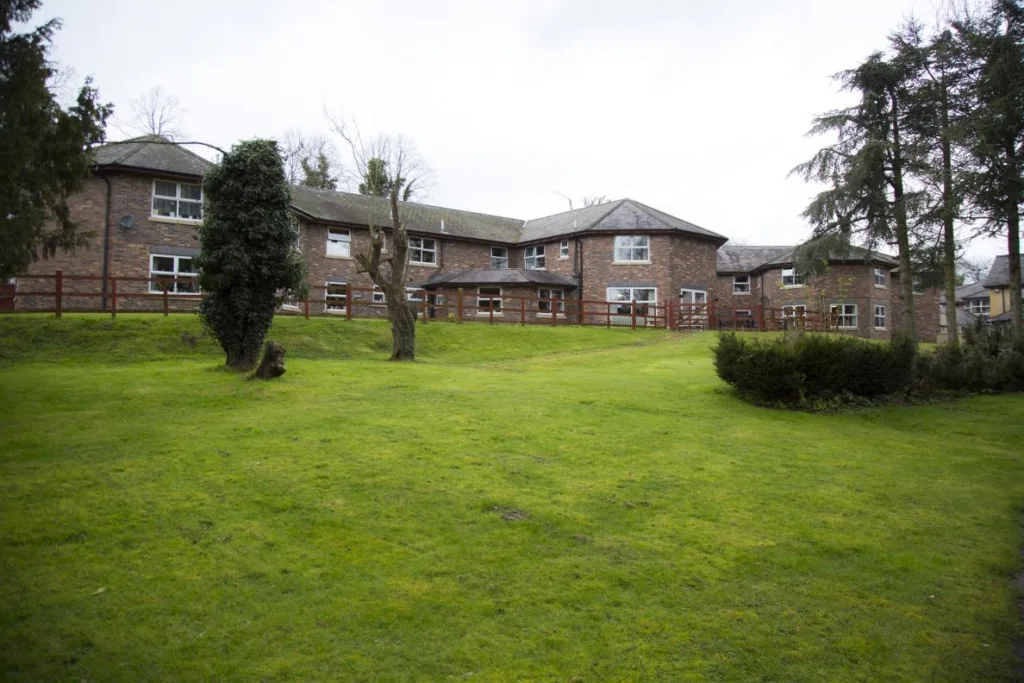 Ashleigh Court Care Home Wrexham viewed from the garden, showcasing the tranquil woodland setting